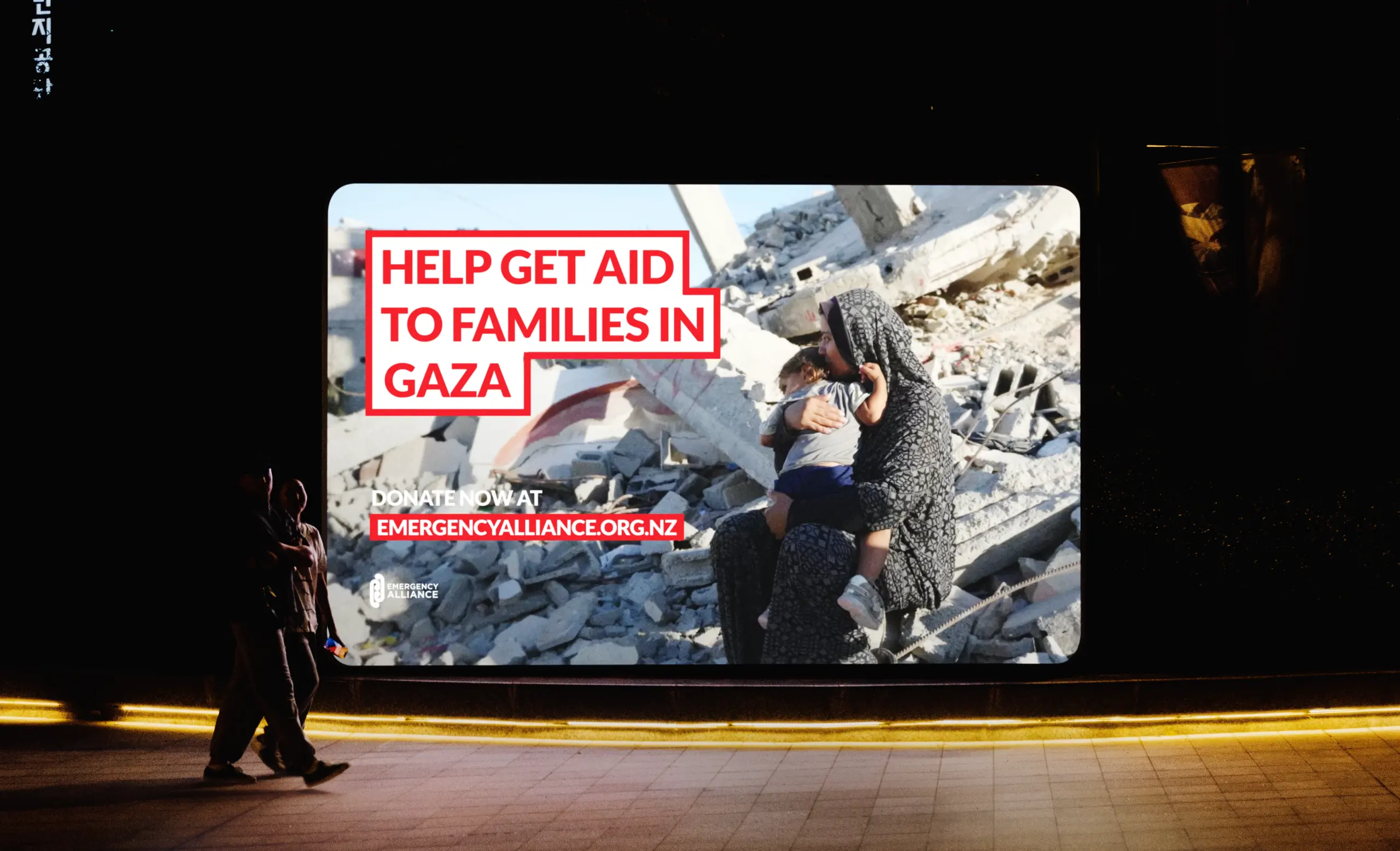 Two people walk by a bright billboard in an underground station