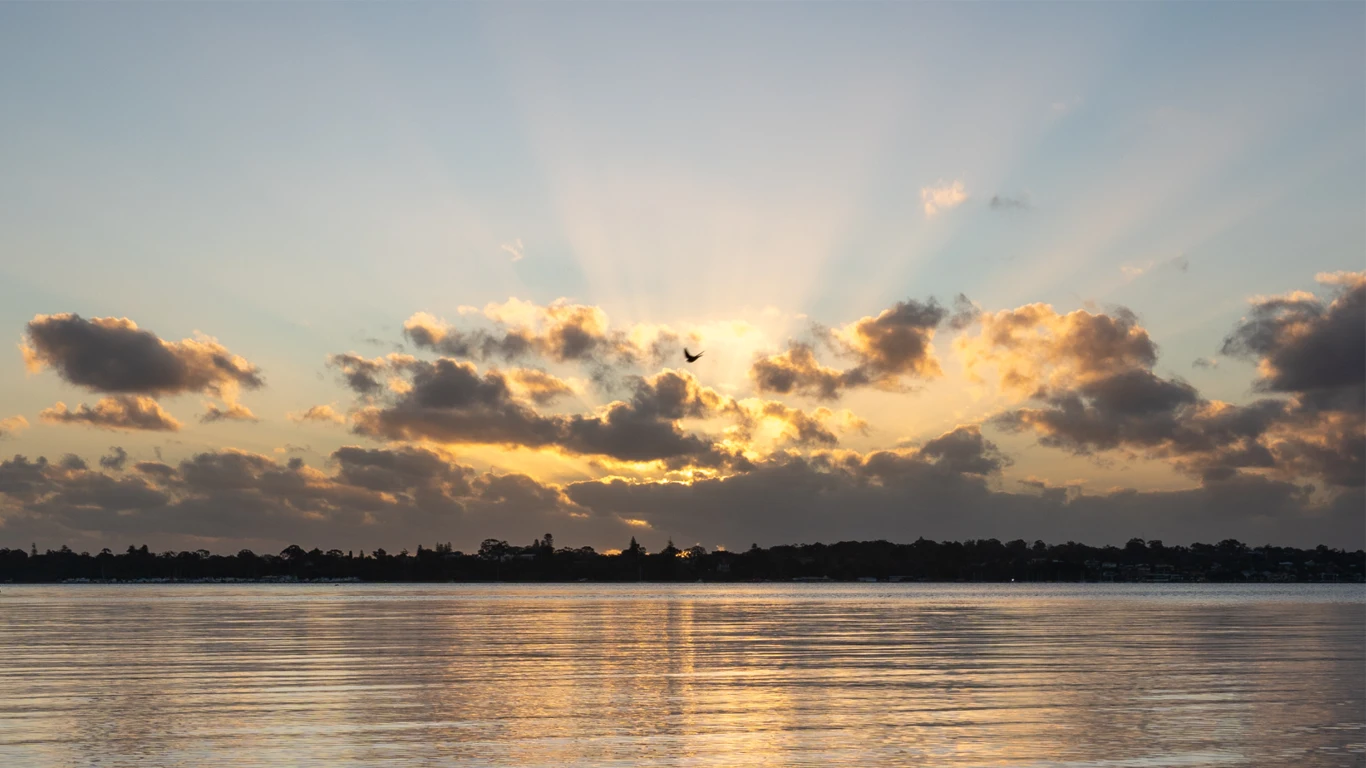 Setting sun shines through the clouds with yellow reflecting from the river below